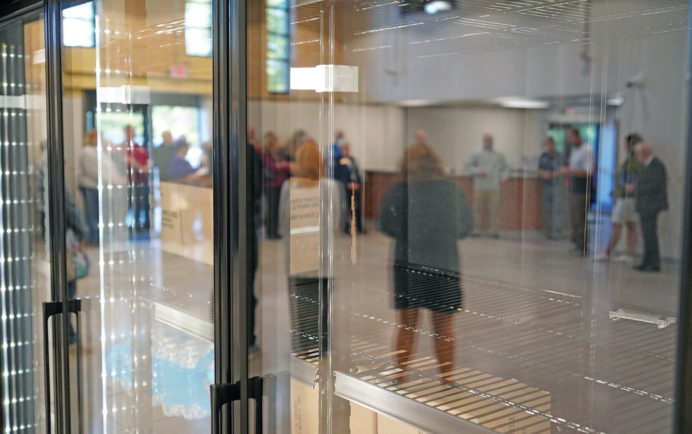 Images of people attending an open house at the new Catholic Charities center are reflected in the glass doors to the refrigerators for the client-choice food pantry that is slated to open in the building later this year. The food pantry occupies part of what was originally a gym for the former LaSalette Seminary.